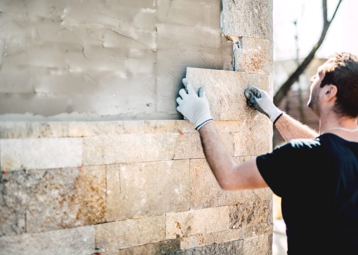 Construction industry worker installing stone tiles on architectural house facade